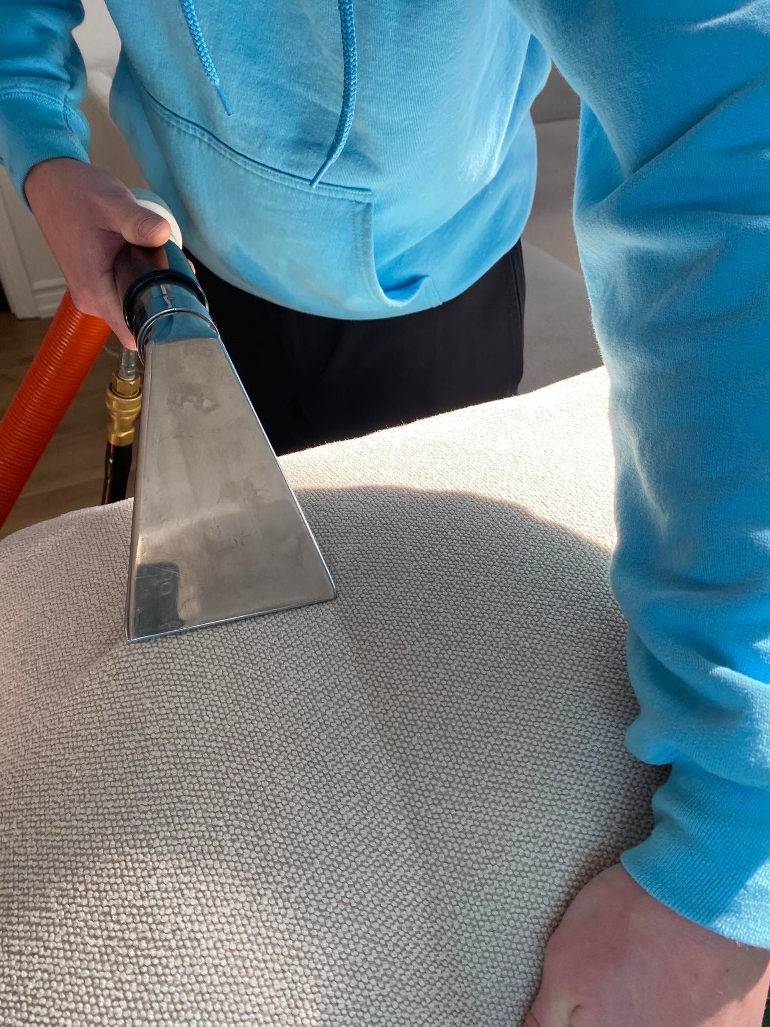 Person using a carpet cleaner nozzle on a light gray rug