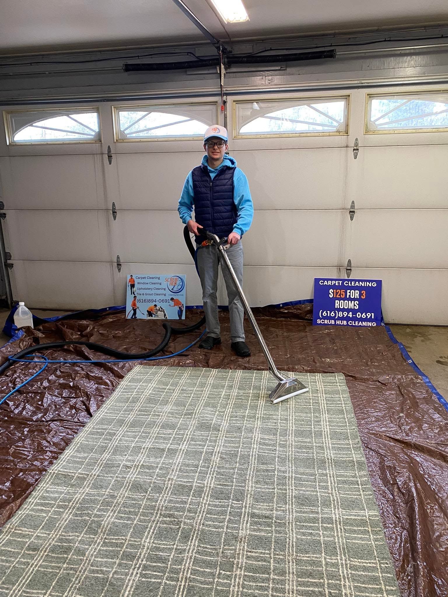 Person using a long-handled tool to rake a large tarp-covered floor in a garage.