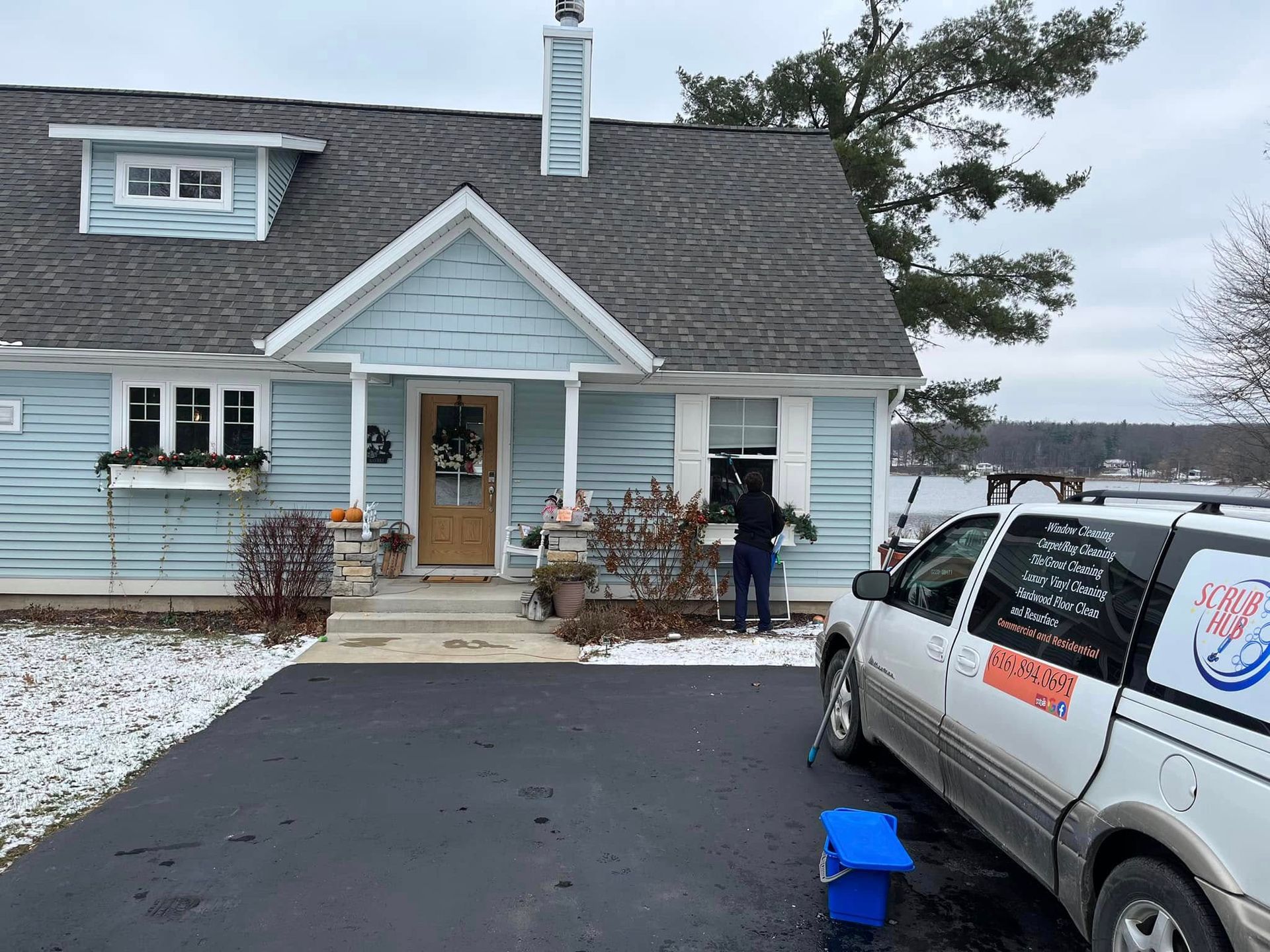 House exterior with snow on the ground, a service van parked in the driveway, and two people by the front door
