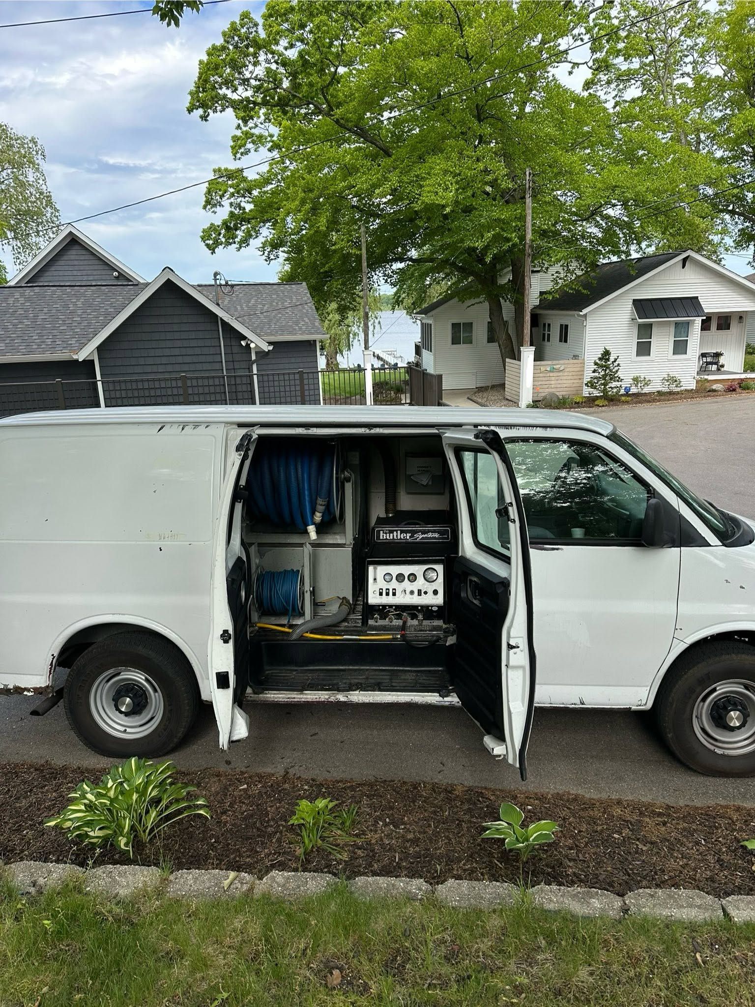 White utility van with side door open, showing tools and equipment parked on a residential street.