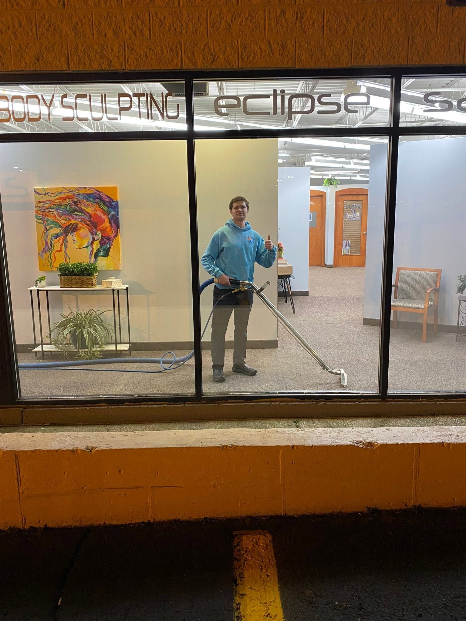Person in a blue shirt mopping a lobby behind large windows at night.