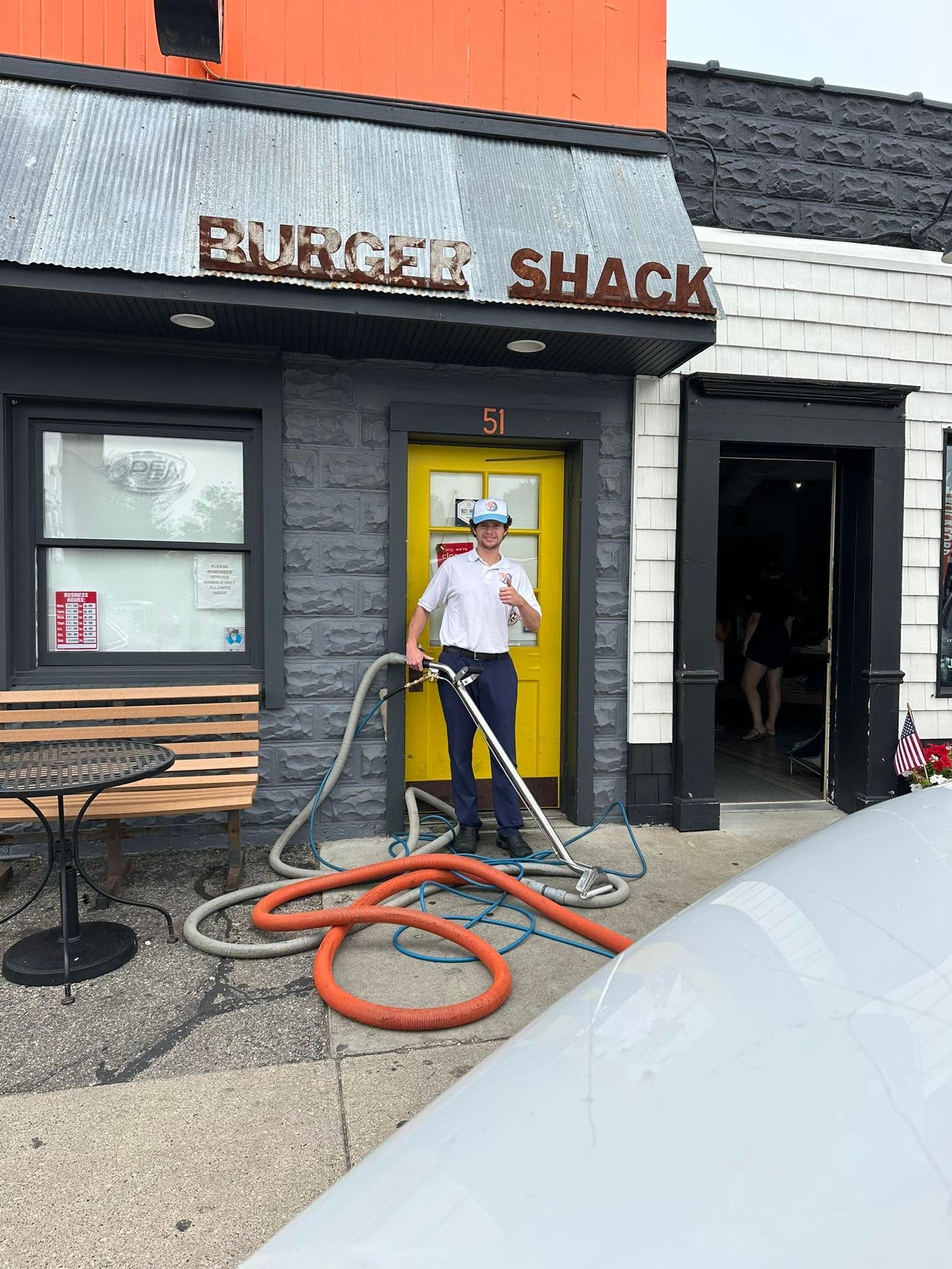 Person vacuuming outside a burger shack with orange hose and yellow door