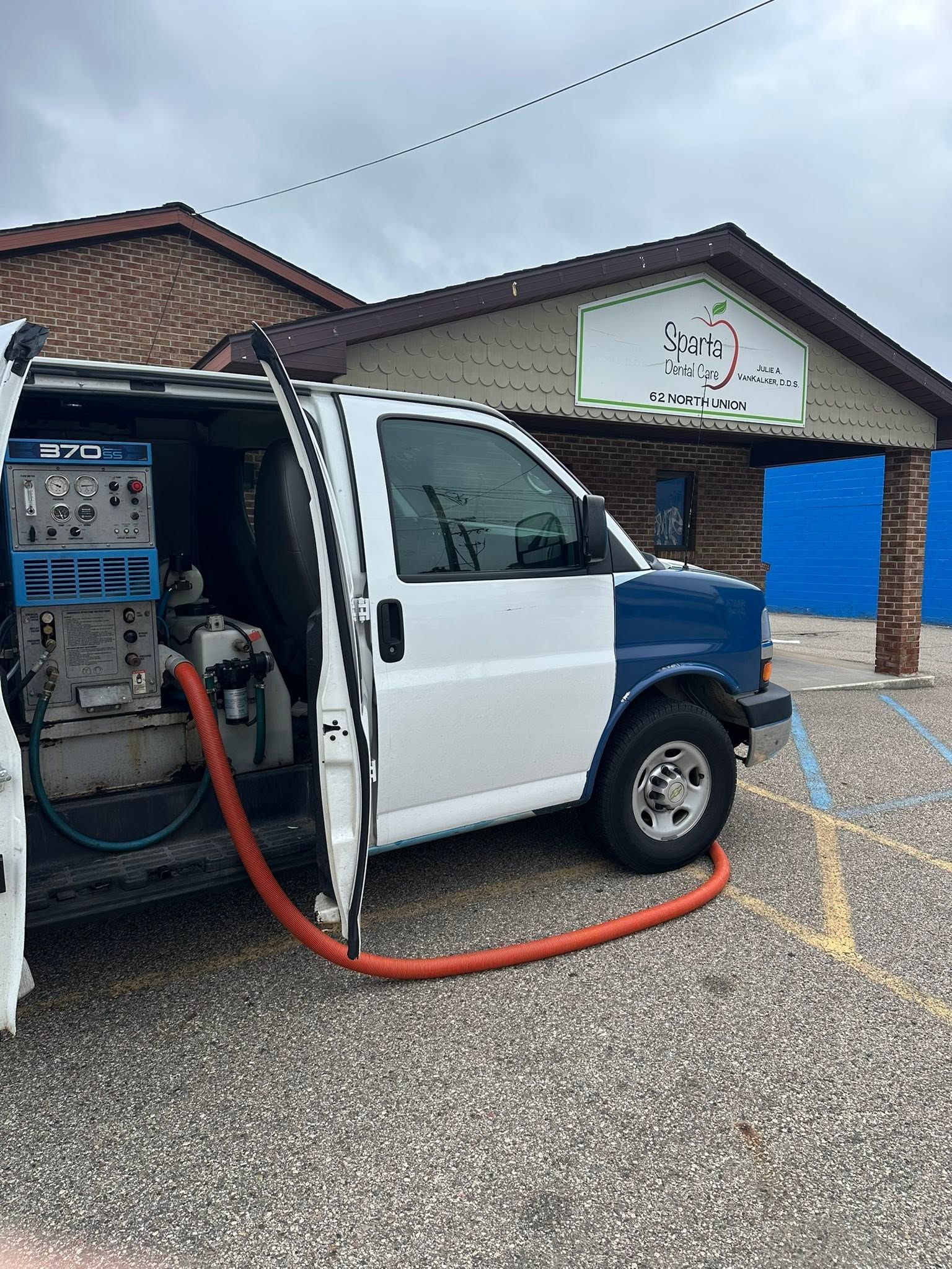 White service truck with open side compartment and red hose parked outside a building on a cloudy day