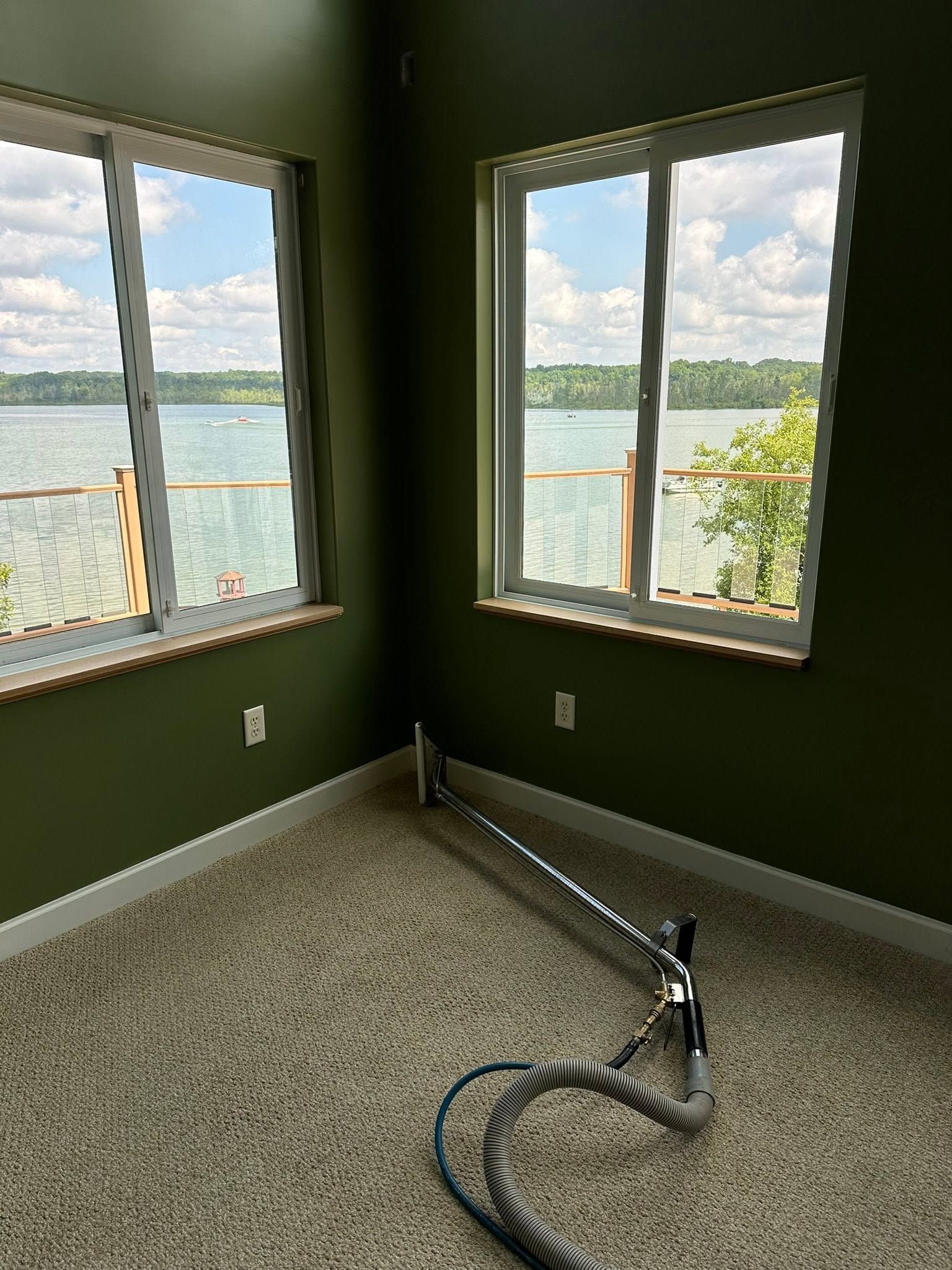 Empty green room with two windows overlooking a lake and a vacuum hose on the carpet.
