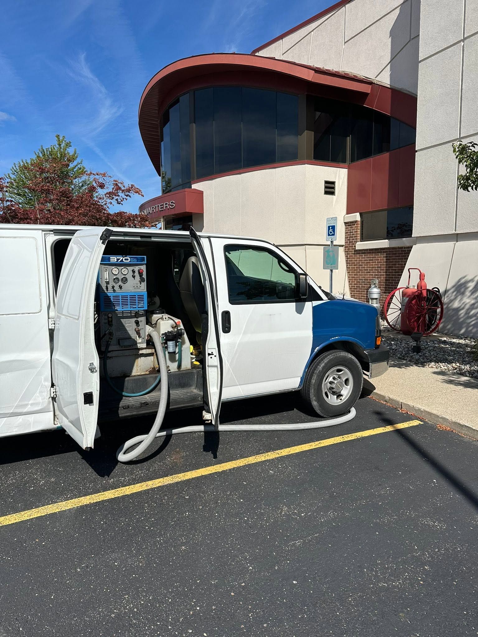 White utility van with equipment parked outside a building, with a person in a wheelchair nearby.