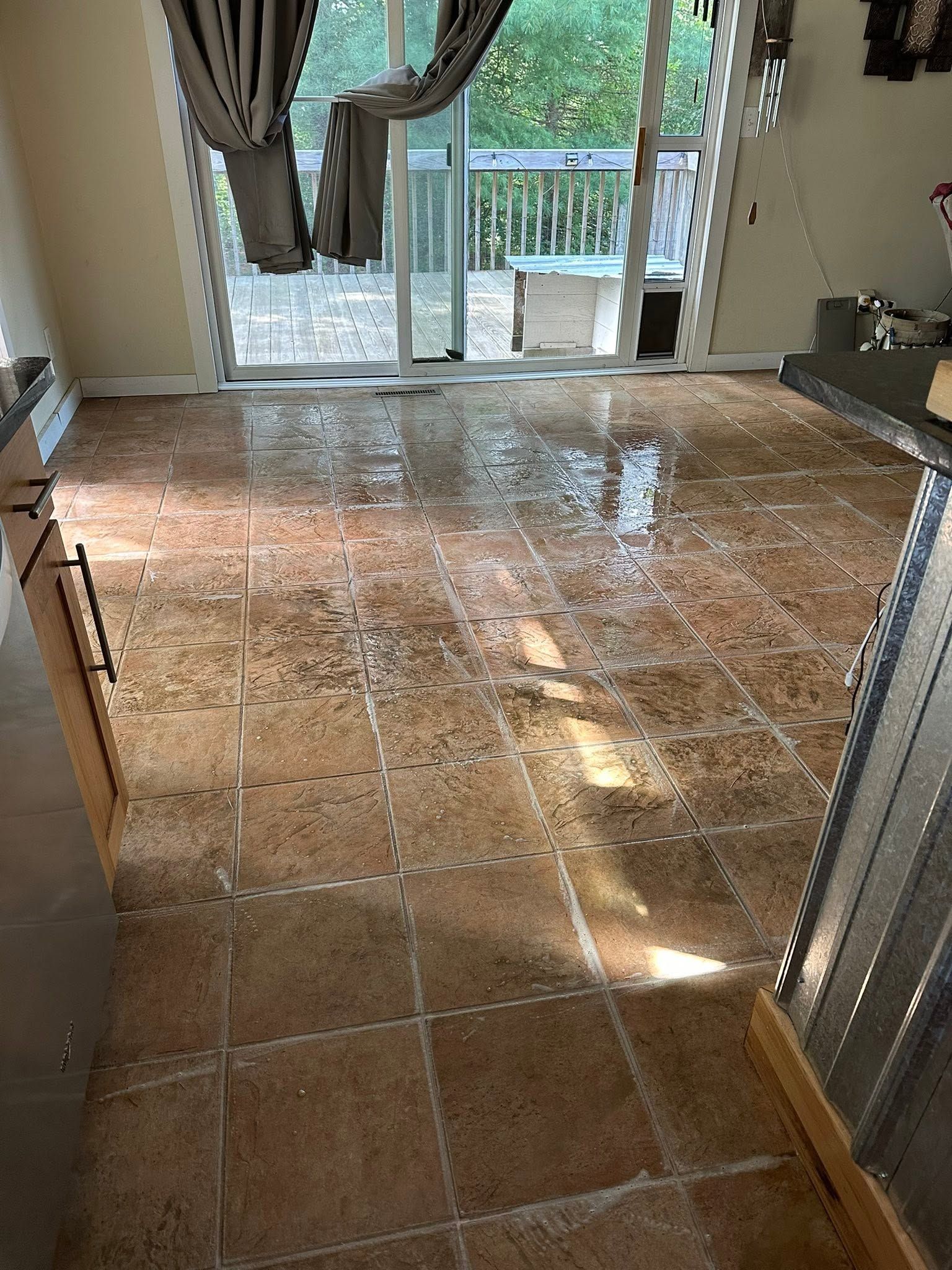 Water-damaged tiled living room floor near sliding glass doors, with curtains and bright sunlight reflecting off wet areas