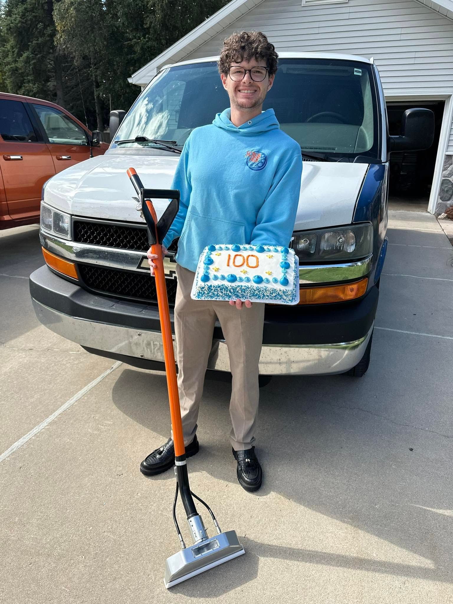 Person holding a box and mop standing in front of a white van in a driveway
