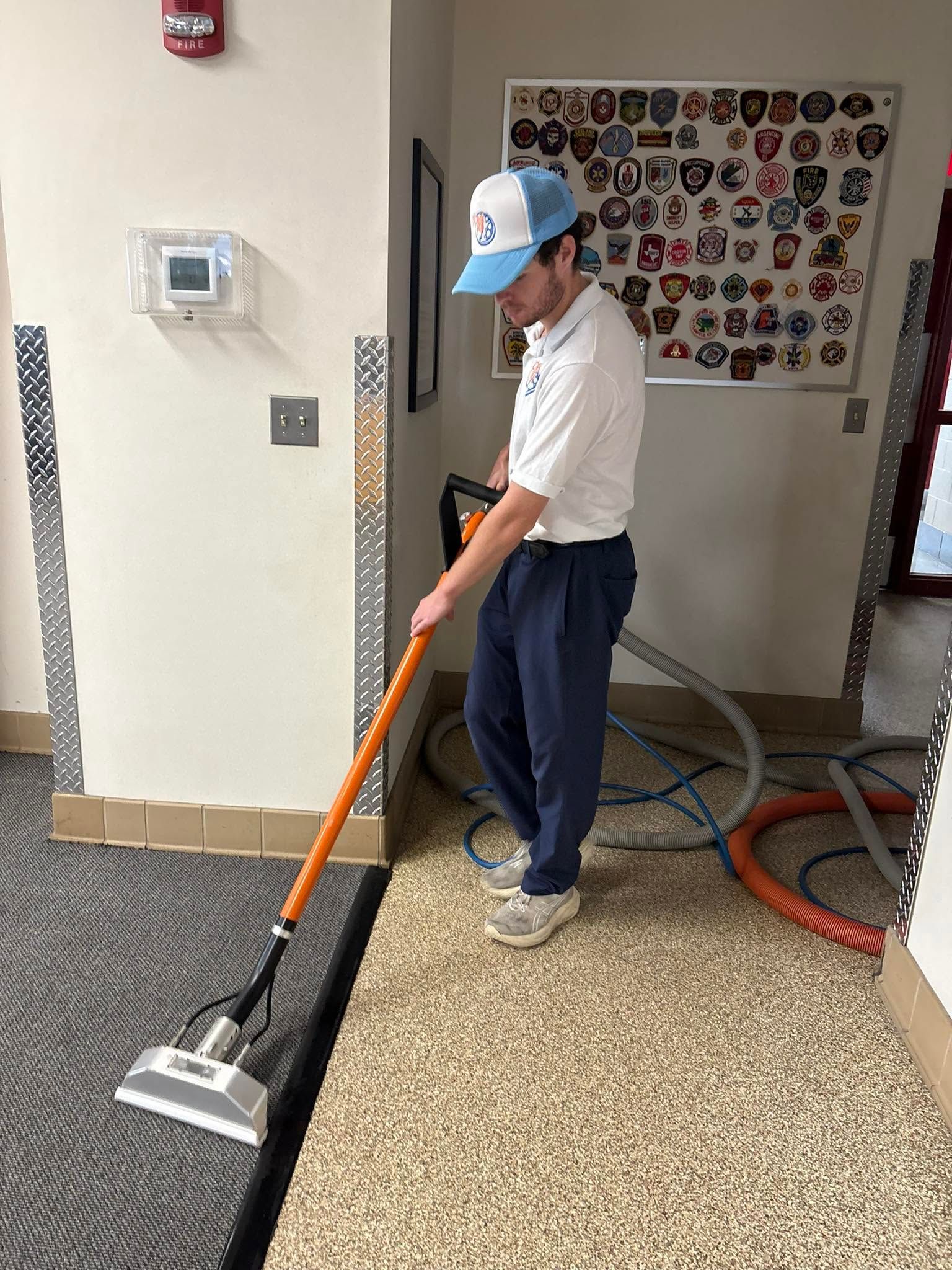 Person vacuuming a hallway floor with an orange vacuum in a school hallway