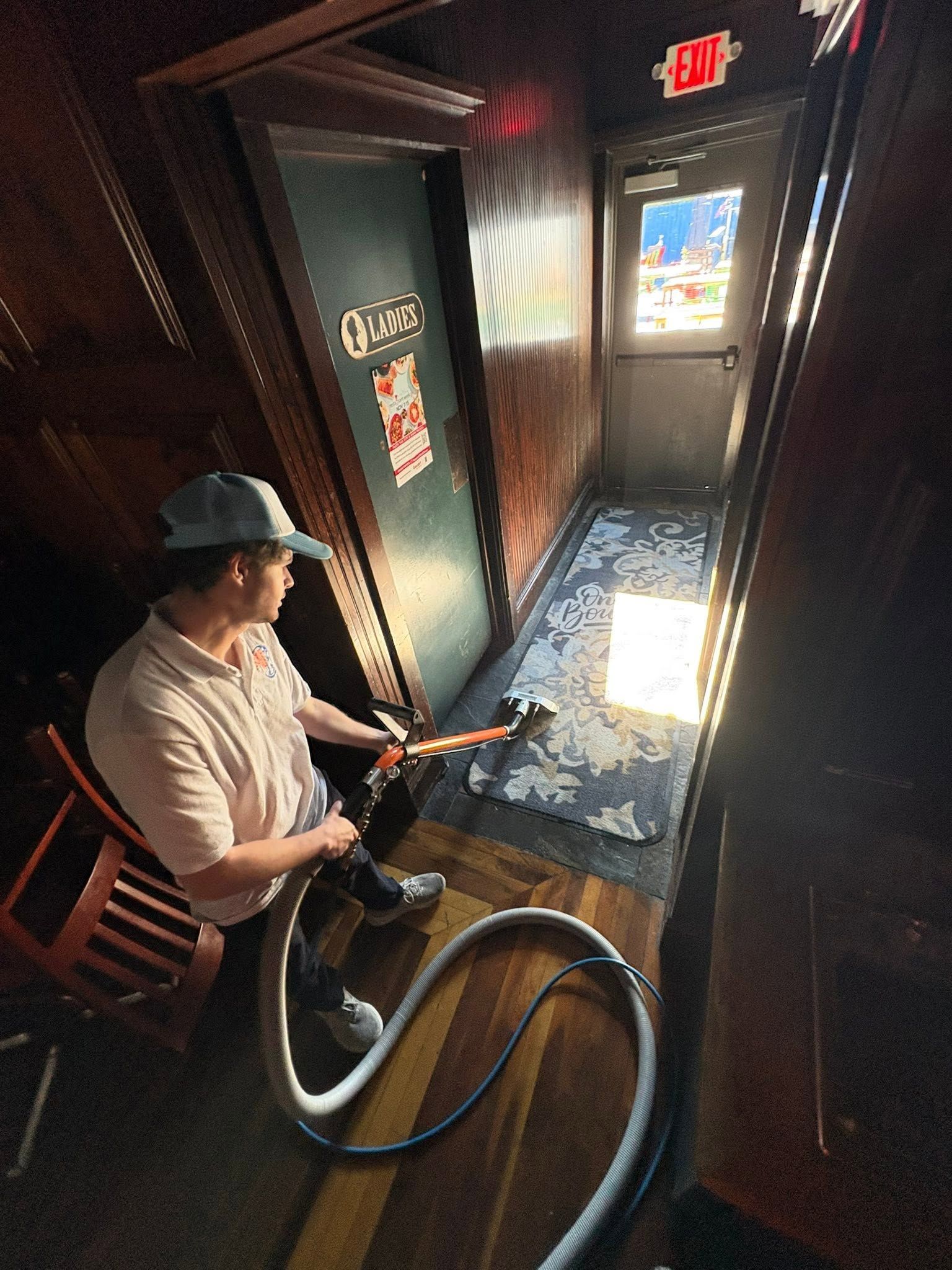 Person holding a hose in a dim hallway, spraying water toward a bright doorway at the end.