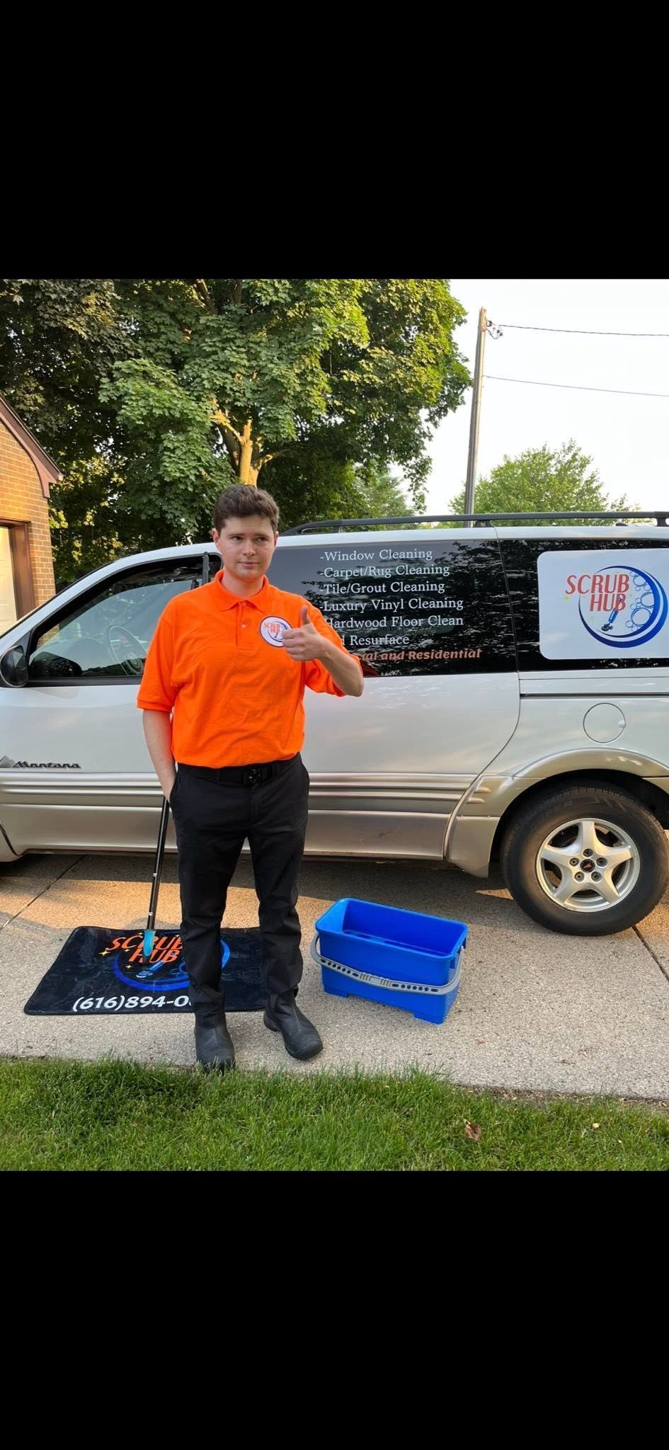 Person in orange shirt stands beside a silver SUV with blue equipment on grass outdoors.
