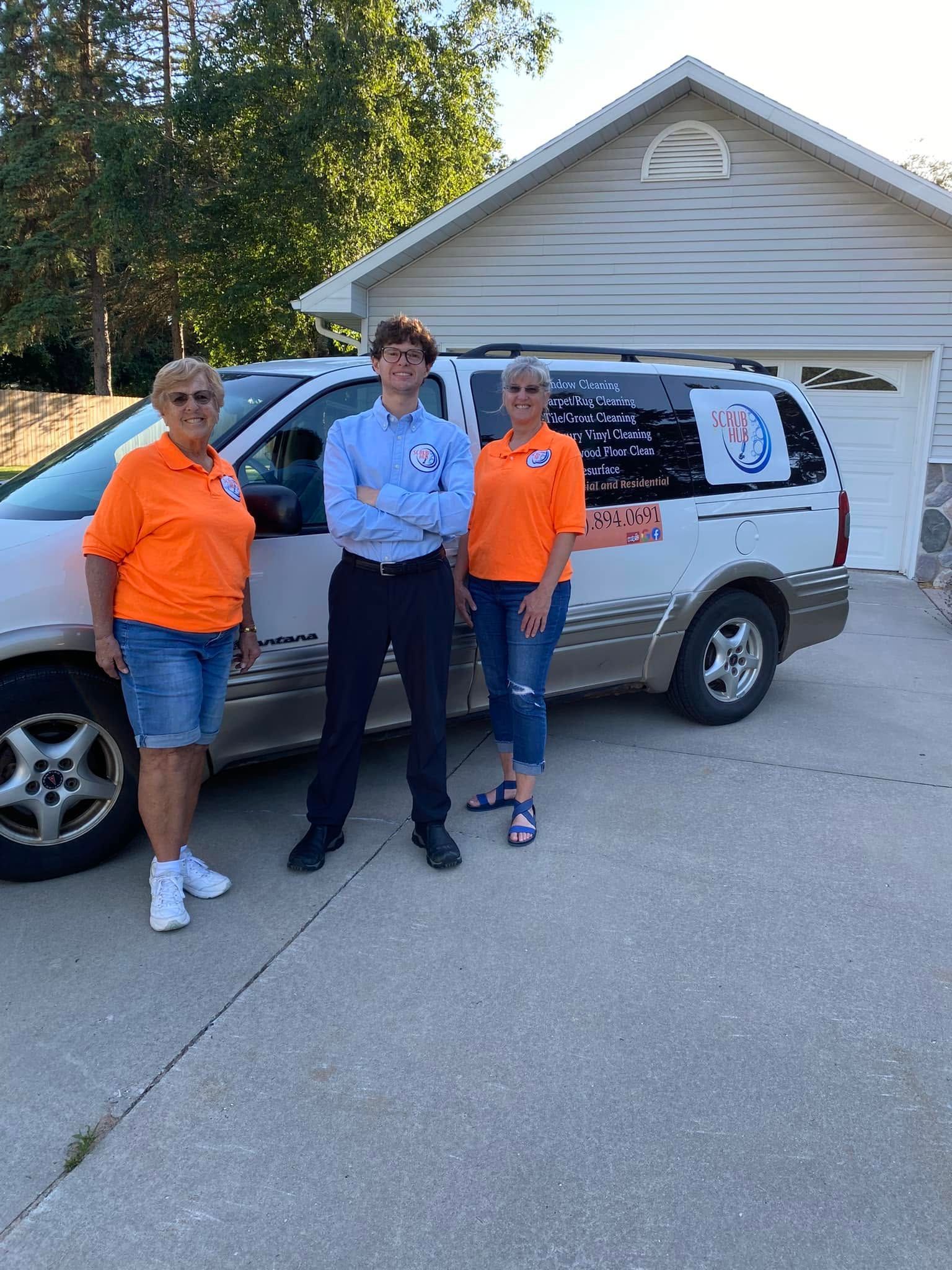Three people standing beside a white van in a driveway, with a house and garage in the background.