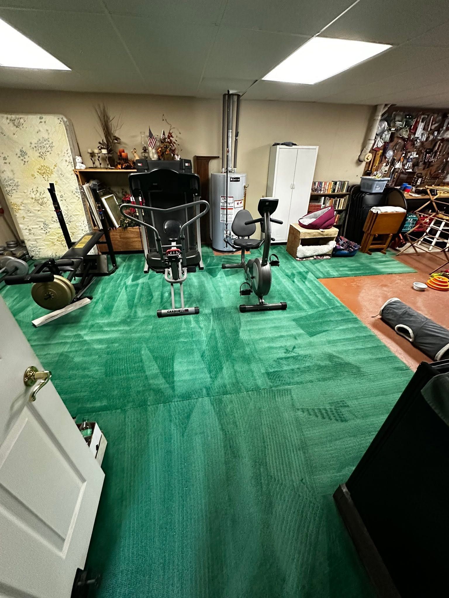 Indoor workout area with green turf, exercise equipment, and weights in a cluttered room