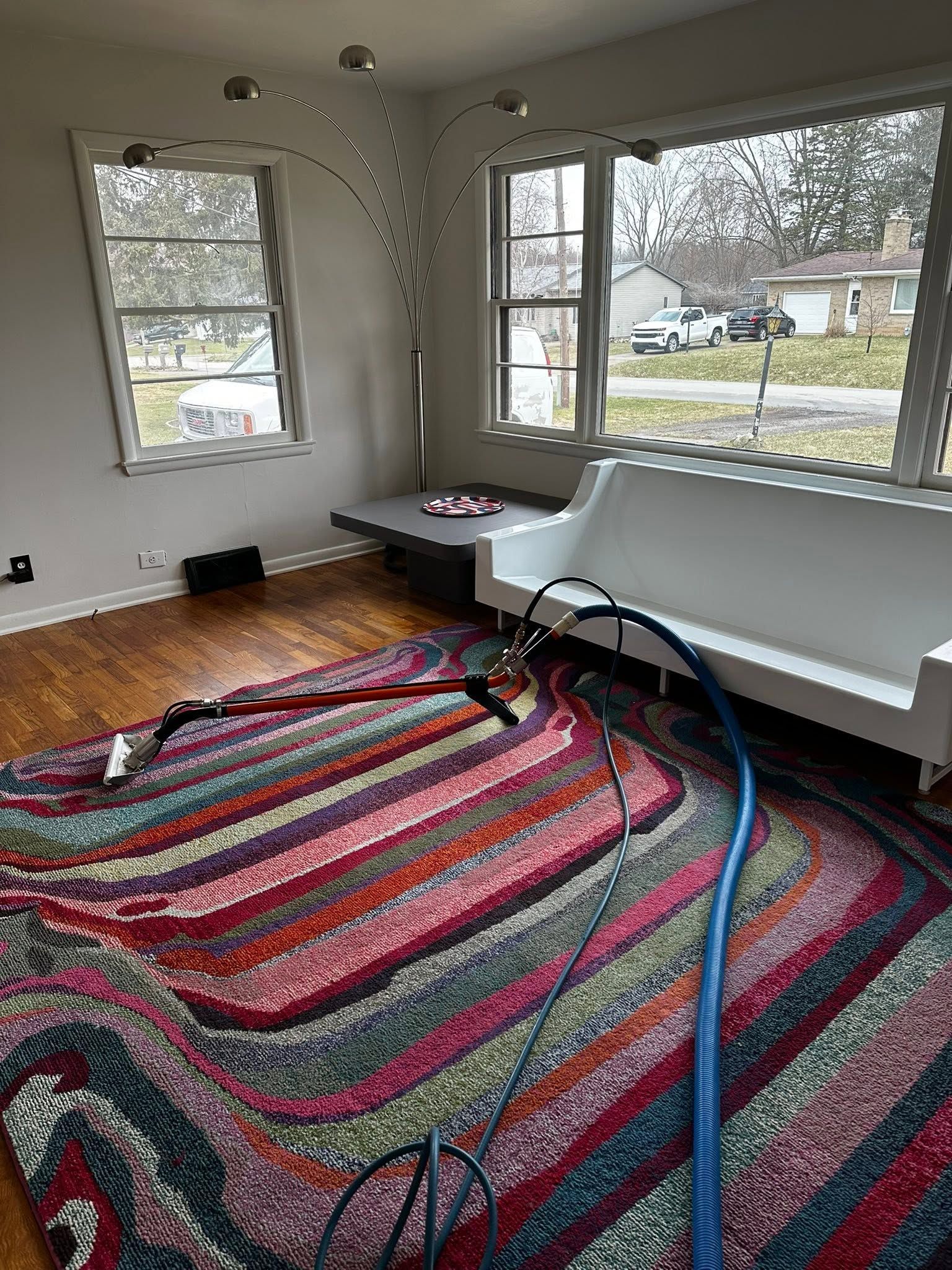Living room with a striped rug, white couch, large windows, and a vacuum hose on the floor