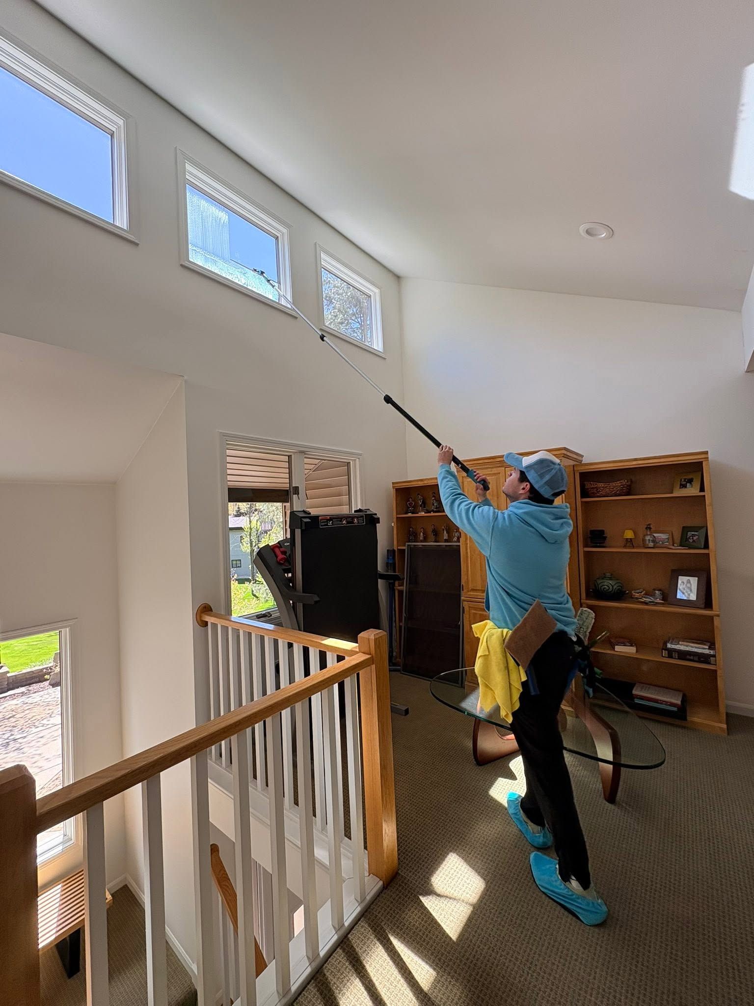 Person in blue costume reaches upward with a long pole inside a bright home hallway.