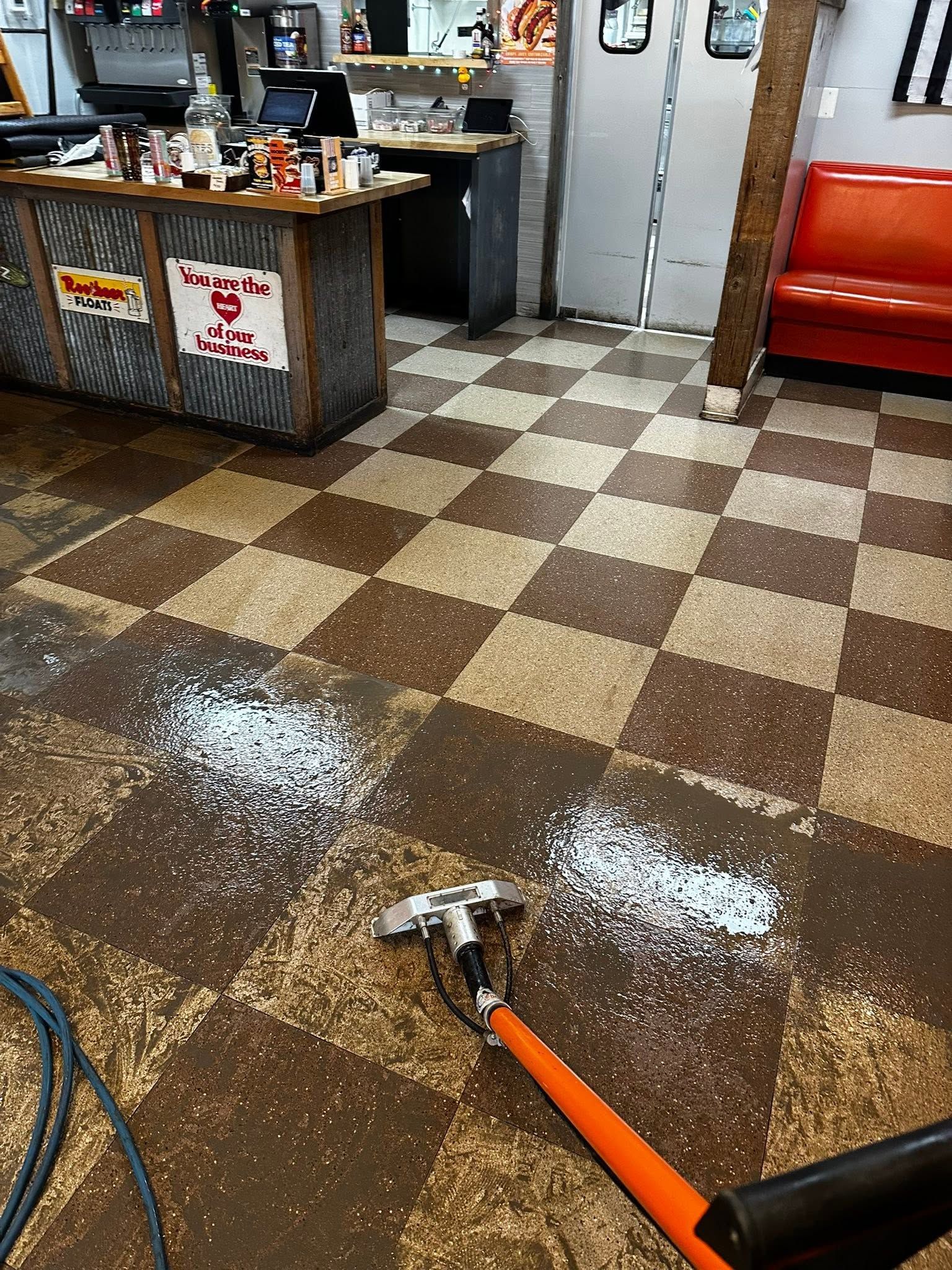 Mop on brown checkered floor with spilled white debris near a counter and red booth.
