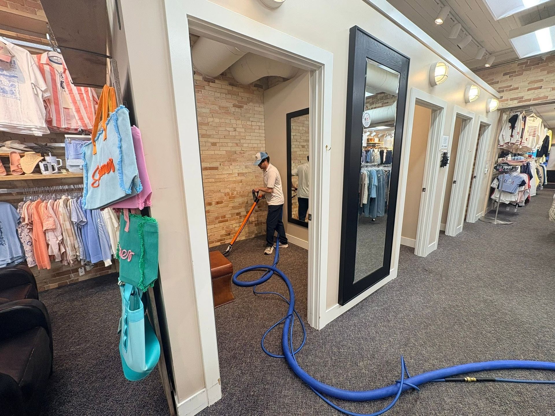 Retail store aisle with open dressing rooms and a person vacuuming the floor