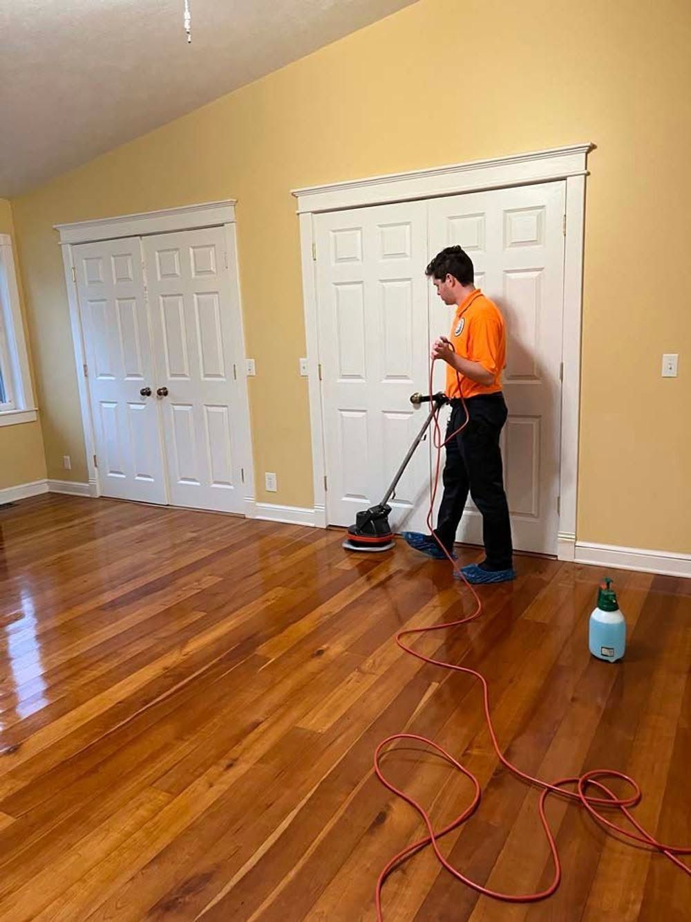 Person polishing a hardwood floor in an empty room with beige walls and white closet doors.
