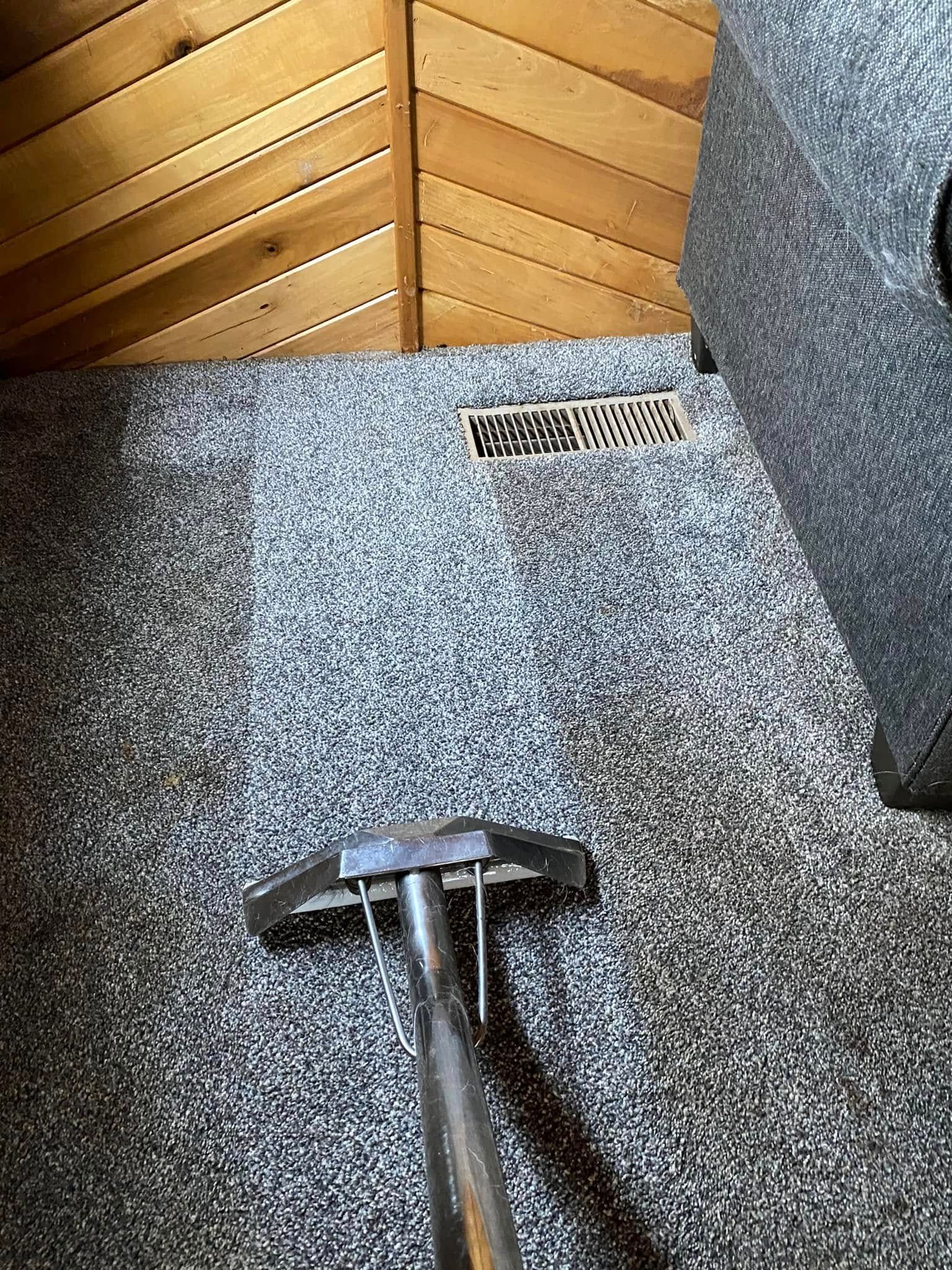 Carpeted floor with a metal handle in the foreground and a wooden panel wall with a floor vent.