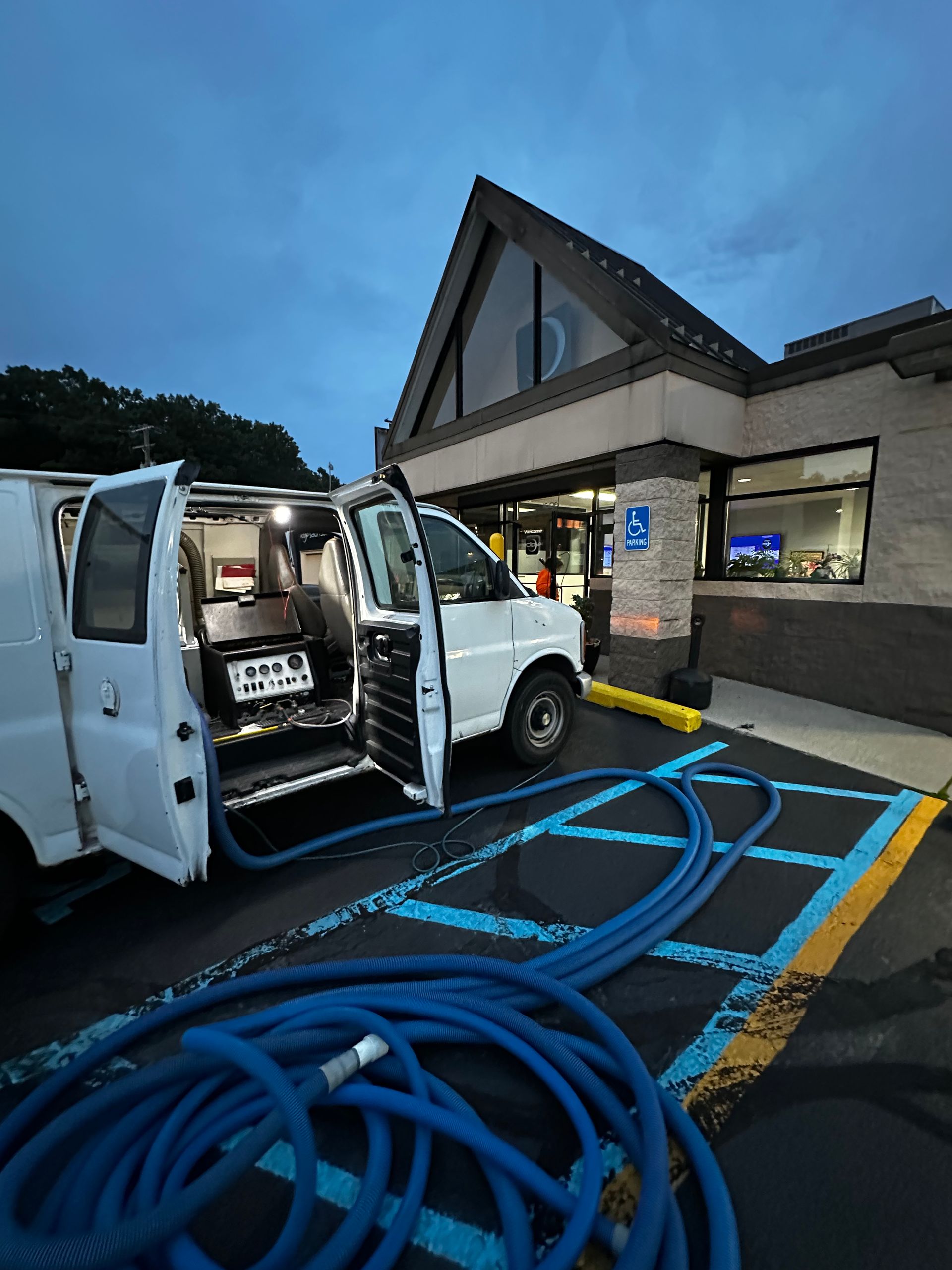 Utility truck with open rear doors beside a building, blue hoses coiled on the ground at dusk.