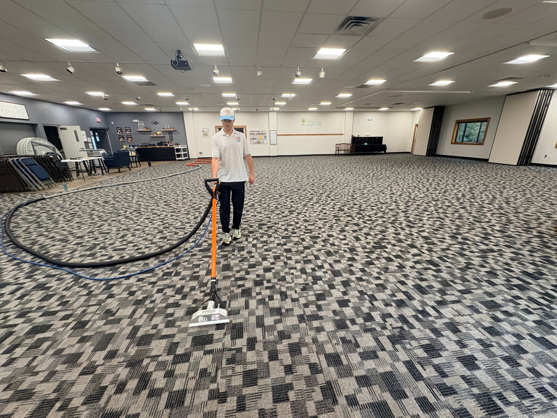 Person standing in a large carpeted hall holding a hose attached to cleaning equipment