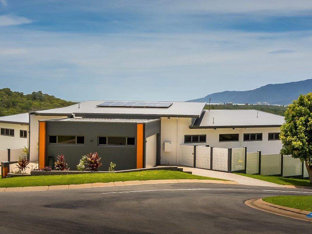 Modern building with orange accents, driveway, and mountain view under a blue sky