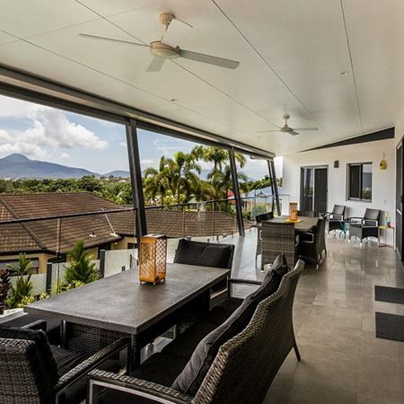 Covered patio dining area with wicker furniture, ceiling fans, and mountain view beyond the railing