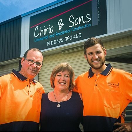 Three people in orange work shirts standing outside Chirio & Sons construction office sign