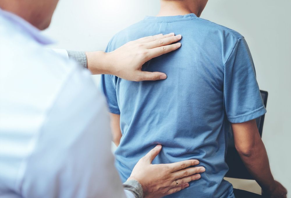 A man in a blue shirt is getting his back examined by a doctor.