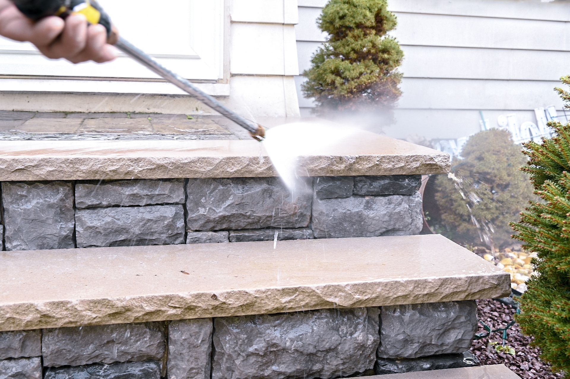 A person is using a high pressure washer to clean a wooden deck.