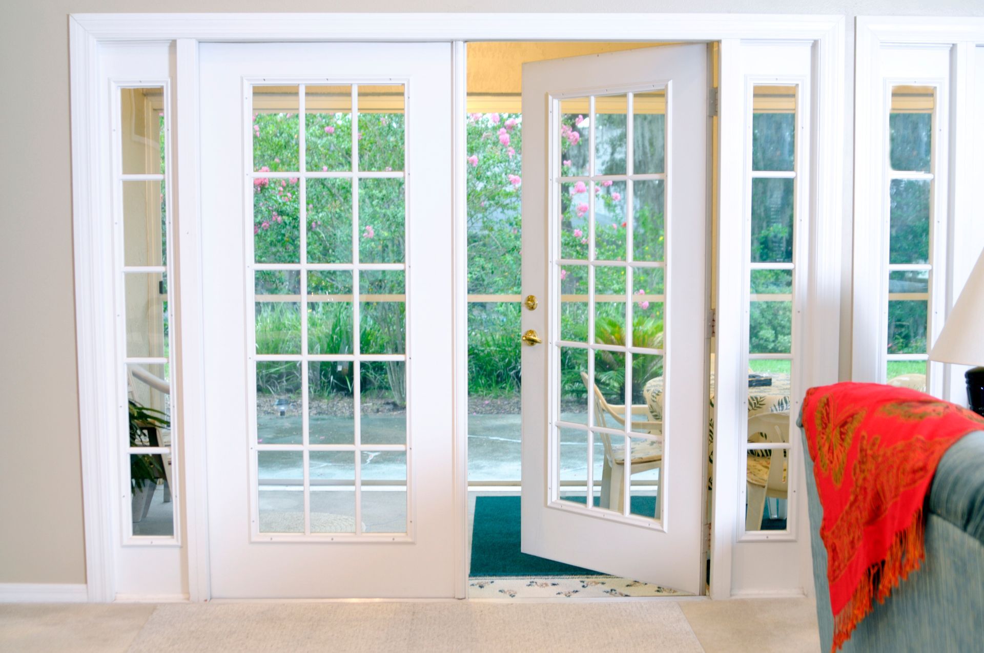 White French doors open onto a green yard, with a couch and decorative throw blanket visible.