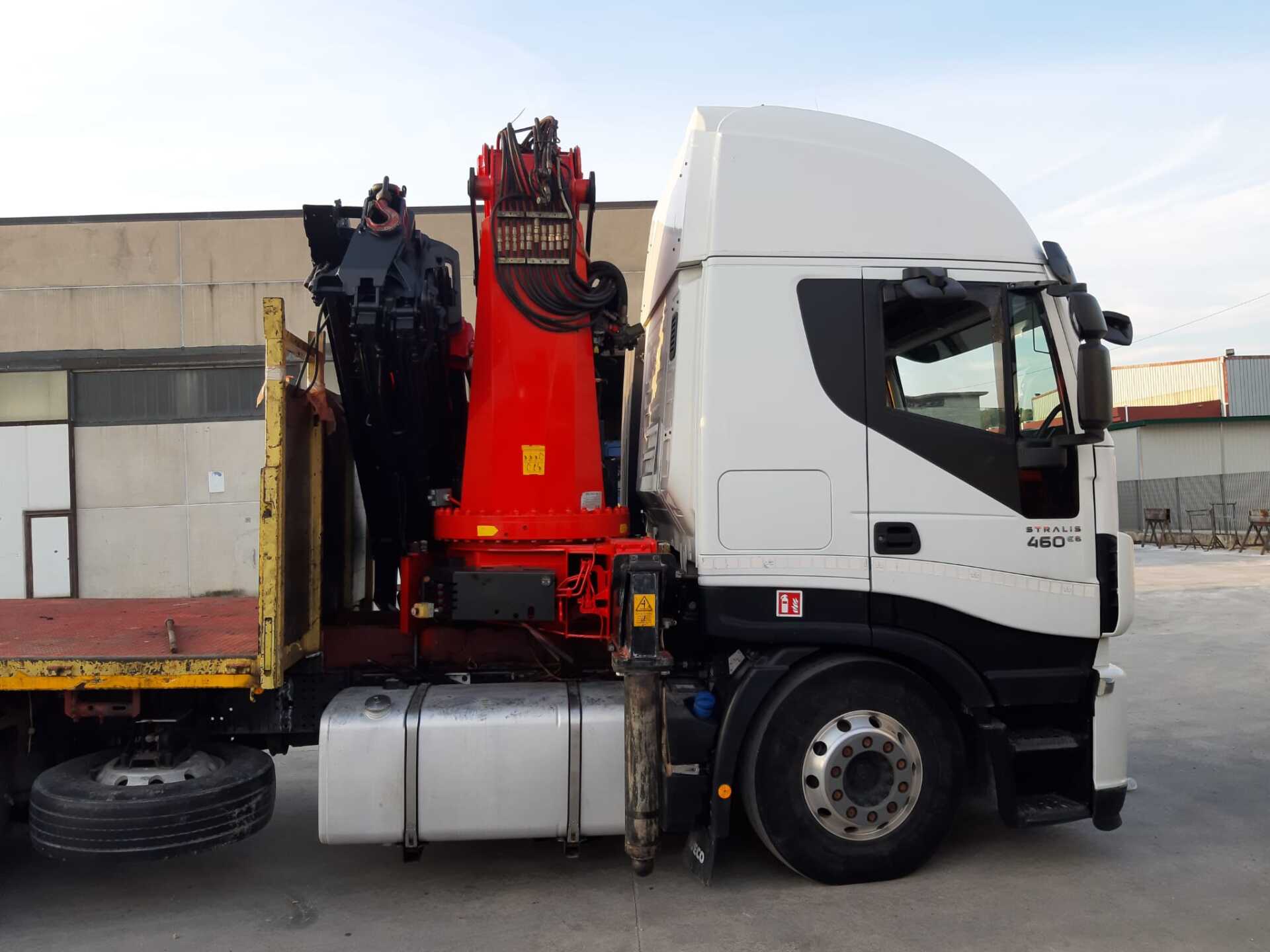 Un camion bianco con una gru rossa sul lato è parcheggiato davanti a un edificio.