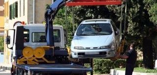 Un'auto viene sollevata da una gru e caricata su un carro attrezzi.