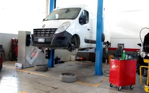 Un furgone bianco è su un ponte elevatore in un garage.
