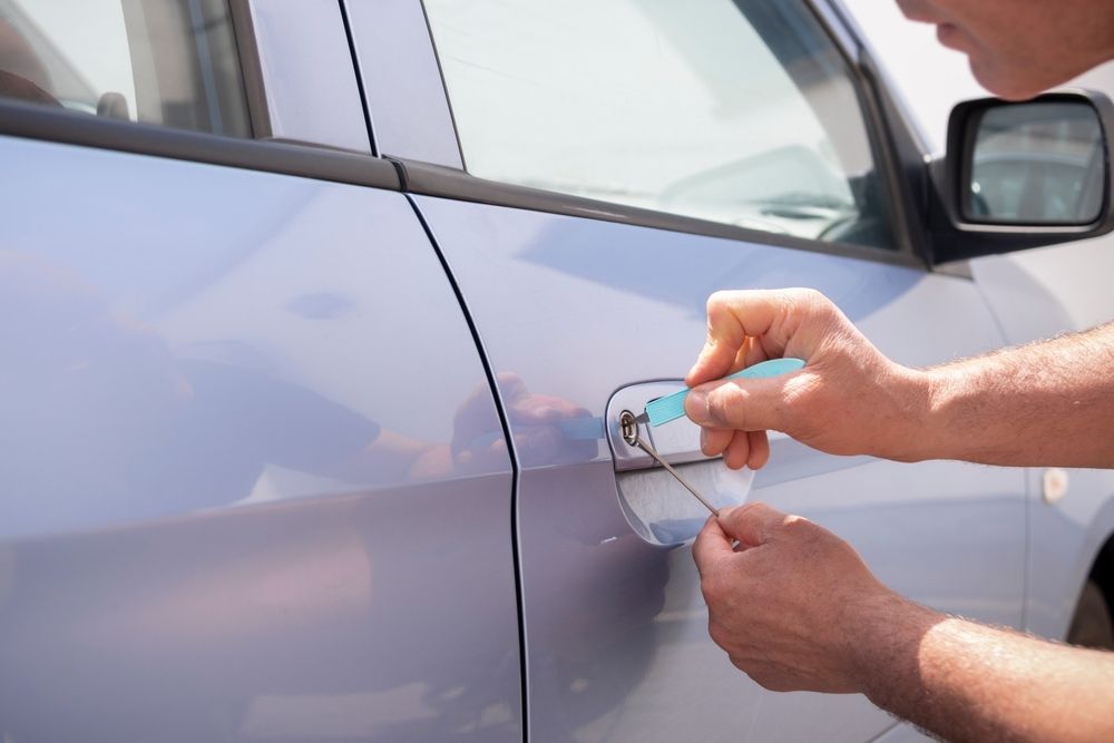 A person uses locksmith tools to pick the lock of a light blue car door.