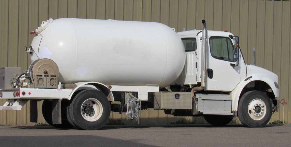 A white tanker truck parked against a light brown corrugated wall.
