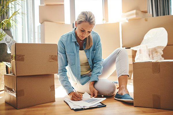 a woman is sitting on the floor surrounded by cardboard boxes and writing on a clipboard .