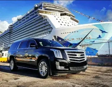 A black suv is parked in front of a large cruise ship.