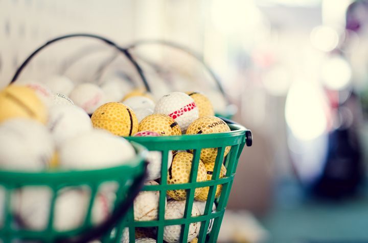 Two green plastic baskets filled with assorted white and yellow golf balls in an indoor setting.
