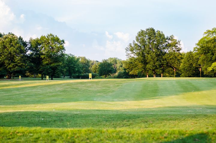 A scenic view of a wide, grassy golf course fairway lined with lush green trees under a bright blue sky.