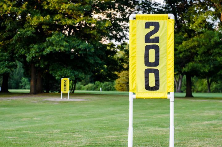 A yellow sign with the number 200 stands on a green golf course, with a smaller, identical sign visible in the distance.