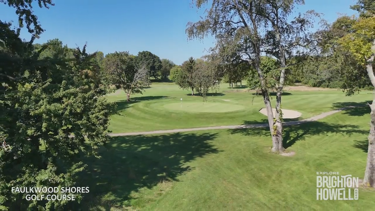 A scenic aerial view of a lush green golf course featuring a putting green, sand trap, and surrounding trees.