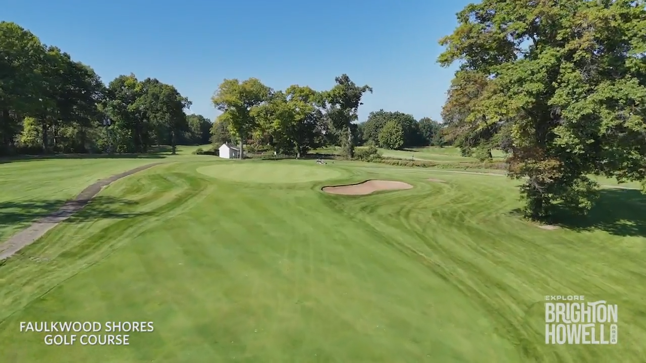 An aerial view of the Faulkwood Shores Golf Course with a green, sand bunker, trees, and blue sky.