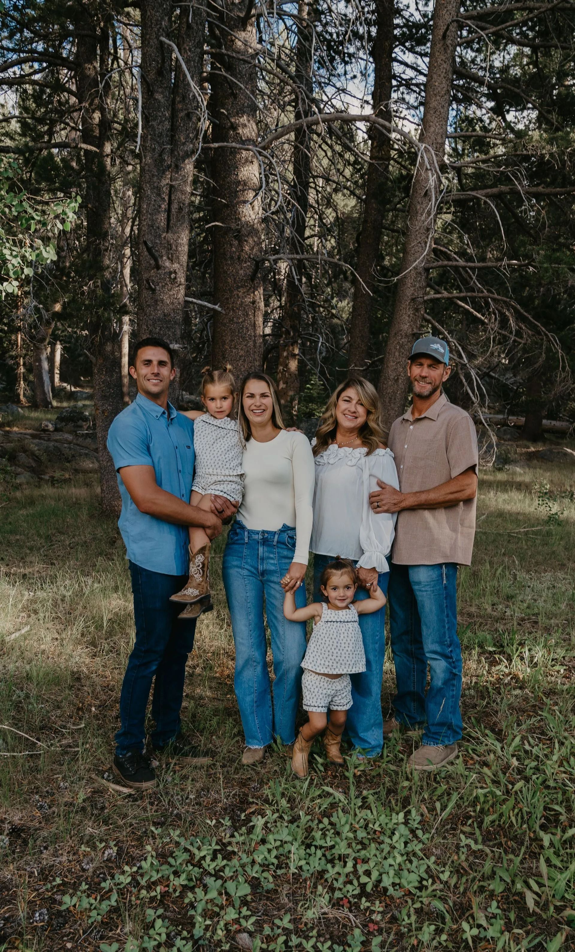 Family of six poses outdoors in a wooded area, smiling.