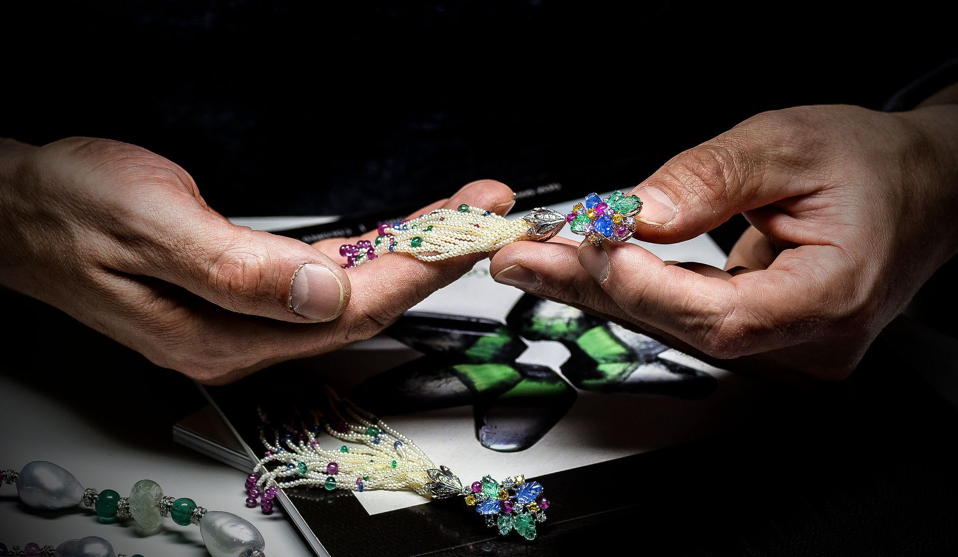 Hands holding a colorful beaded bracelet over a dark table with jewelry-making supplies
