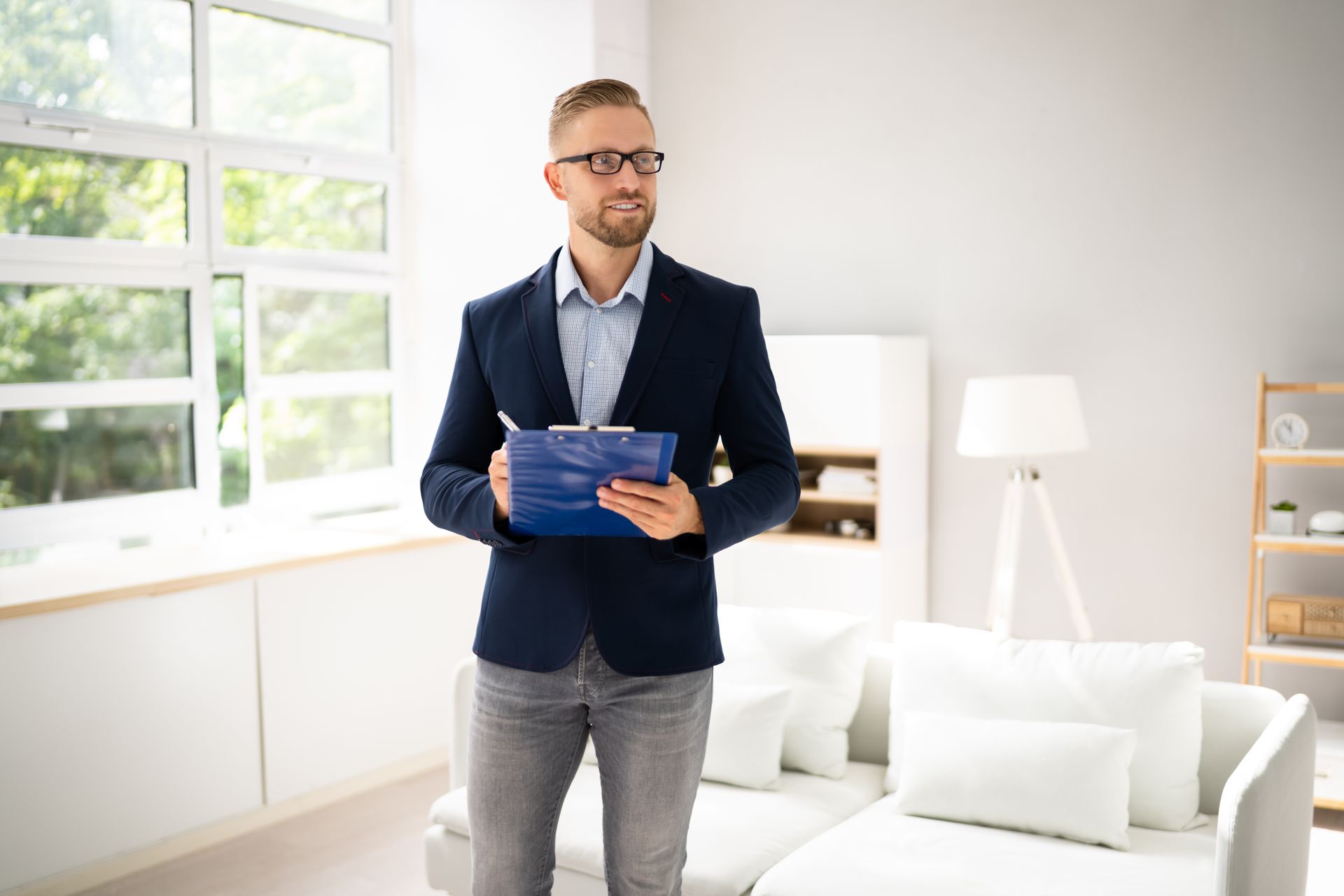 Man holding a blue folder in a bright living room with white furniture and large windows