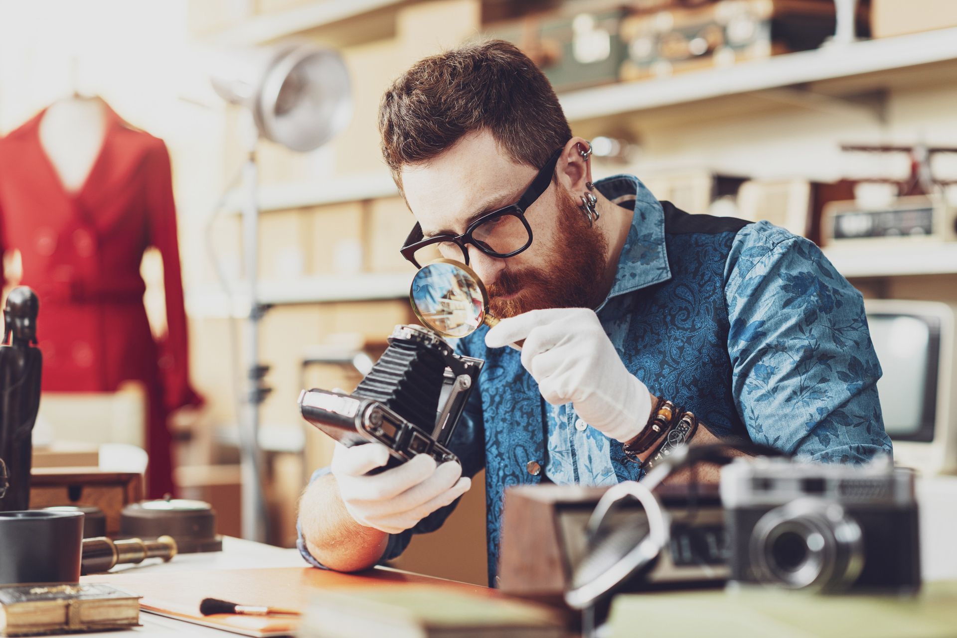 Person inspects vintage camera with magnifying glass in an appraisal shop setting. Person inspects vintage camera with magnifying glass in an appraisal shop setting.