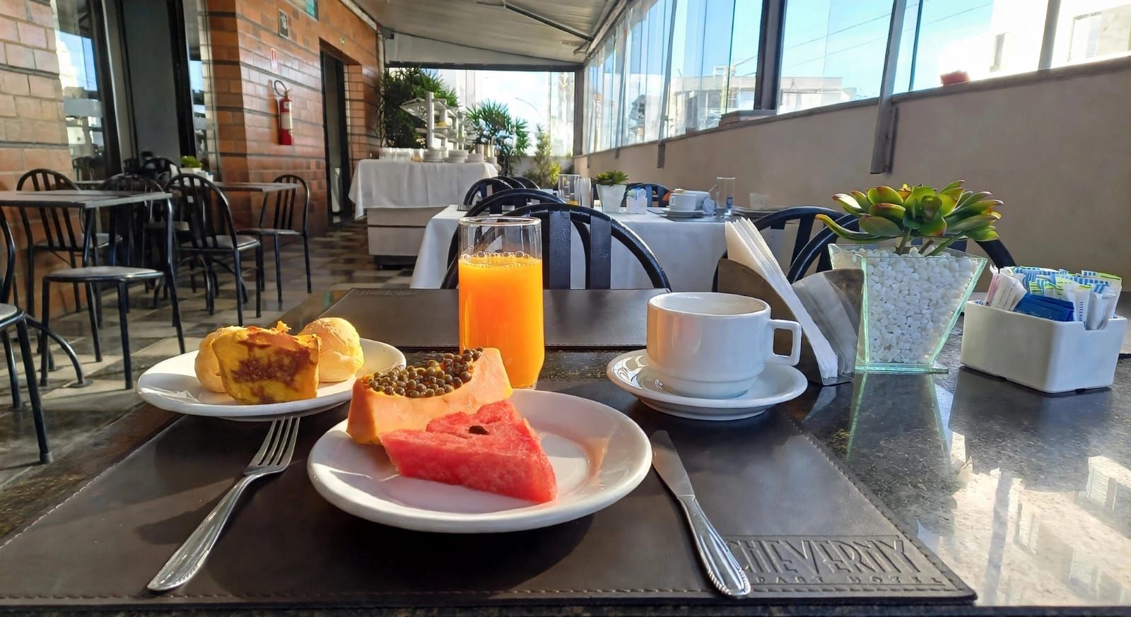 Pequeno-almoço servido numa mesa de café, com fruta, pastelaria, sumo de laranja, café e um porta-guardanapos.