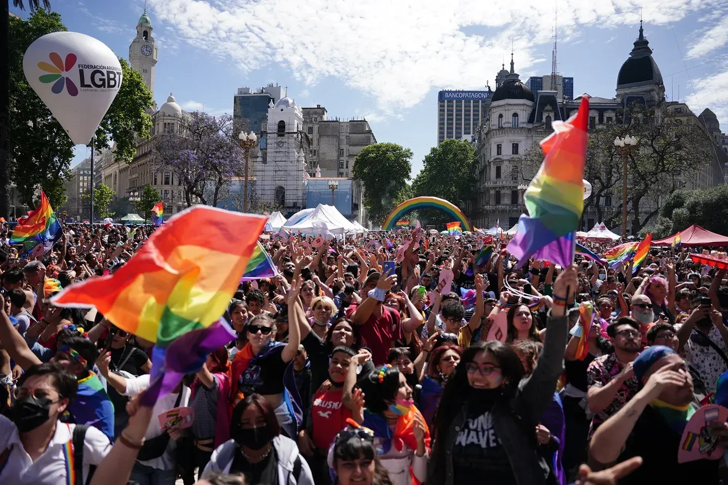 Crowd at a Pride parade in Buenos Aires, Argentina, waving rainbow flags under a bright sky.