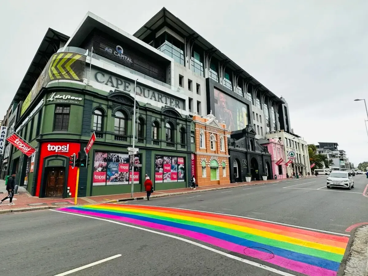 Street with rainbow crosswalk, colorful buildings, and a modern building. Cape Town