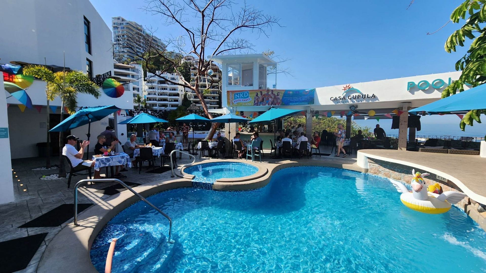 Resort pool with people lounging under shade, a swim-up bar, and clear blue water under a sunny sky Casa Cupula